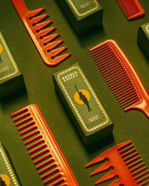 Orange combs and green boxes of rosemary hair oil on a green background