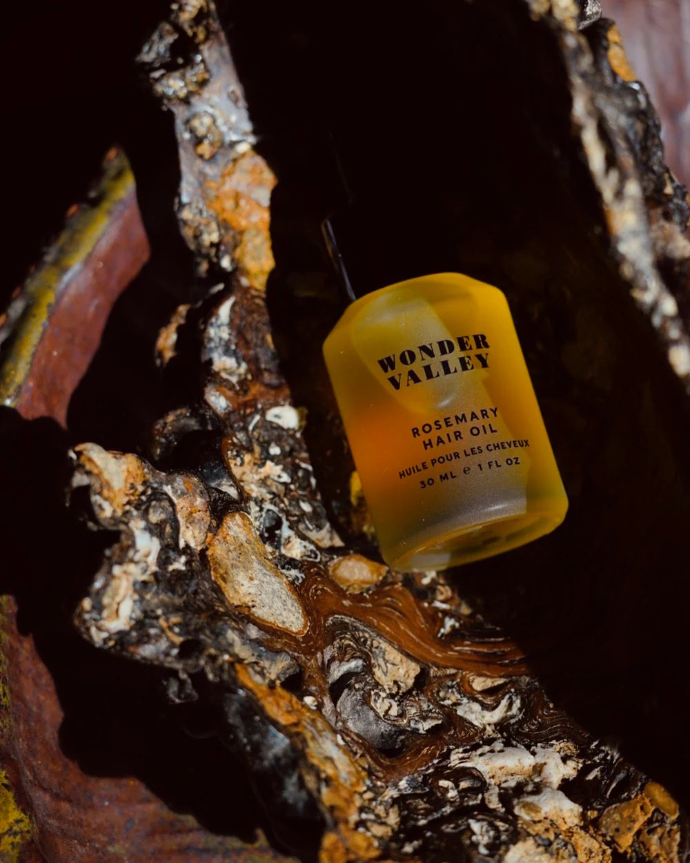Yellow bottle of Wonder Valley Rosemary Hair Oil on a textured surface