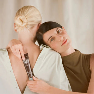A woman with dark hair and a green dress holds a bottle of ROZ evergreen styling cream