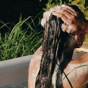 Person washing their hair in a bathtub with greenery around
