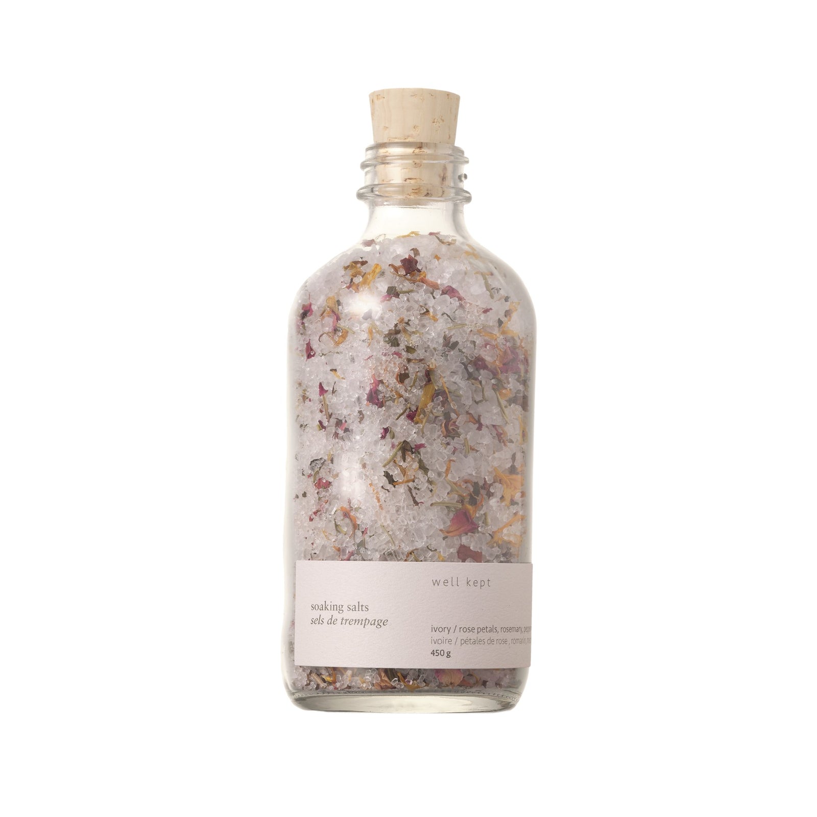 A clear glass bottle with a cork stopper, filled with pink and white floral bath salts. The label reads 'Well Kept' and indicates the size as 450g.