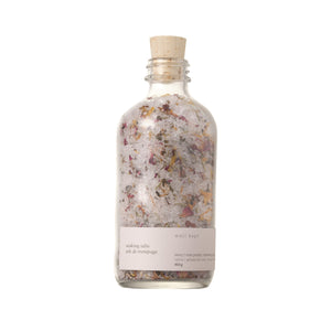 A clear glass bottle with a cork stopper, filled with pink and white floral bath salts. The label reads 'Well Kept' and indicates the size as 450g.