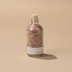 A bottle of Rose soaking salts on a peach background. 
