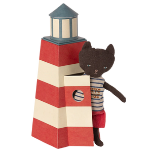 A toy cat figurine in a lifeguard outfit standing next to a striped lifeguard tower that is designed to look like a lighthouse.