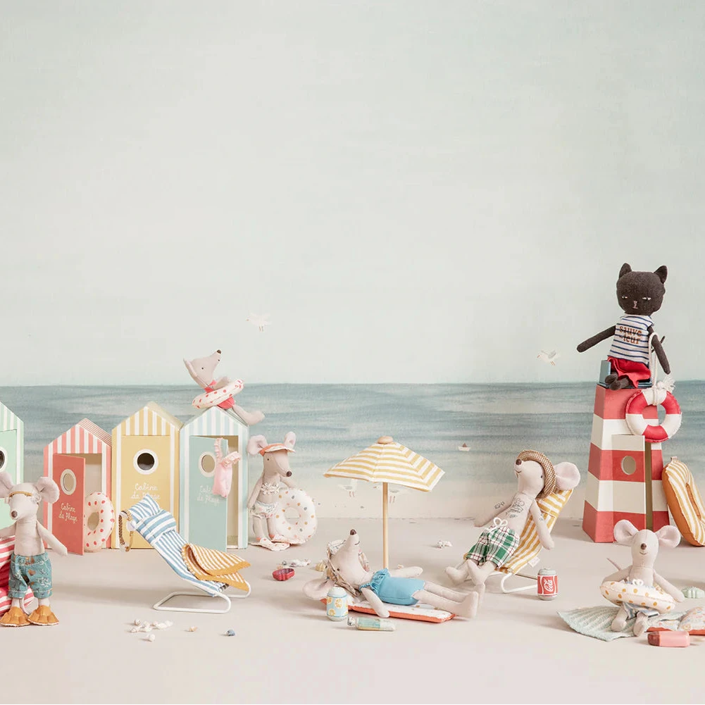 A toy cat figurine in a lifeguard outfit standing next to a striped lifeguard tower that is designed to look like a lighthouse.