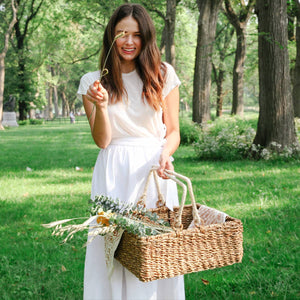 A woman in a park carrying a Savar Handwoven Wicker Storage Basket .