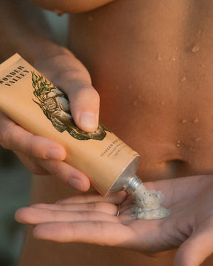 Hand applying seaweed scrub to a person's arm with a visible brand label.