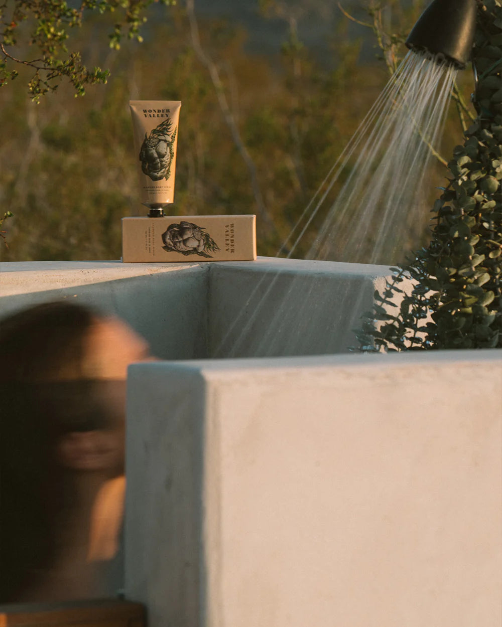 Outdoor setting with a shower head and a tube of seaweed scrub on a ledge.