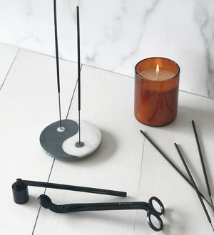 Incense holder with incense sticks and a lit candle on a white surface