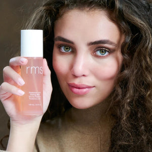 Woman holding a RMS beauty product with a neutral background