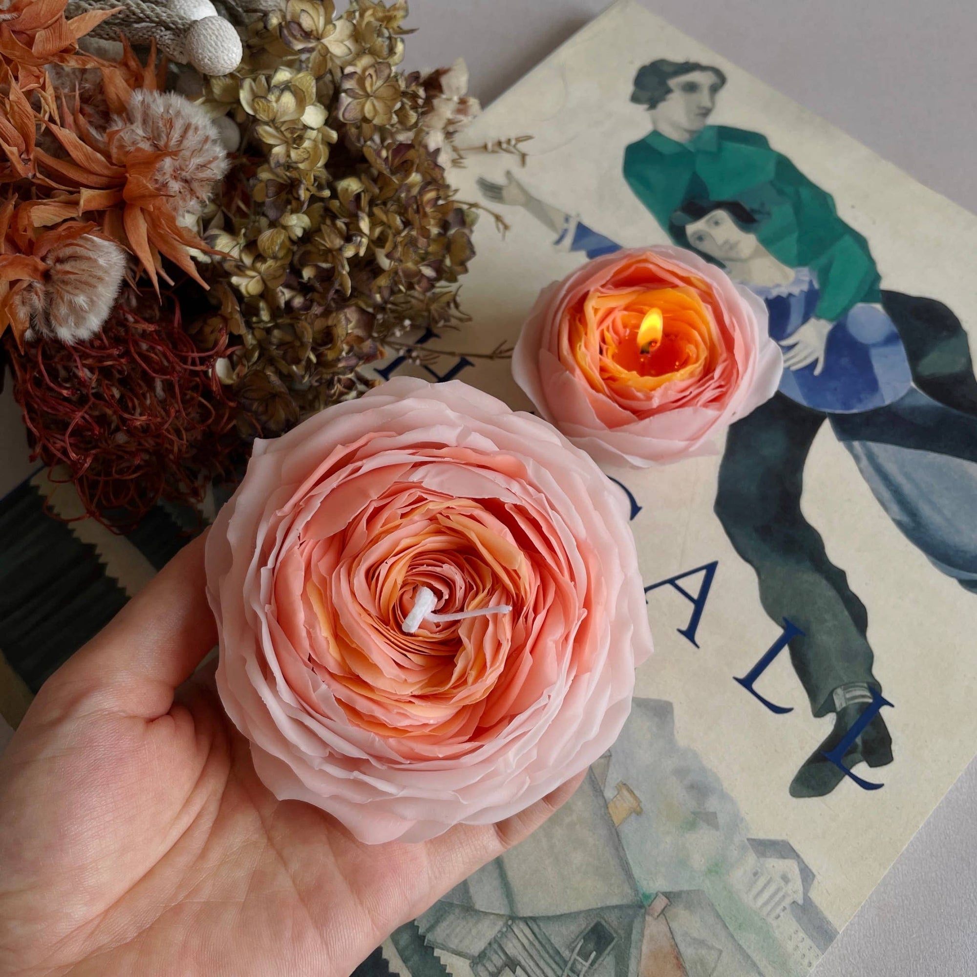 Hand holding a pink rose with a candle, placed on a vintage book