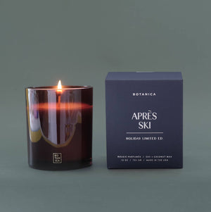 Candle with a lit wick next to its packaging on a dark background