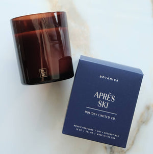 Brown glass candle and 'Apres Ski' Botanica candle packaging on a marble surface