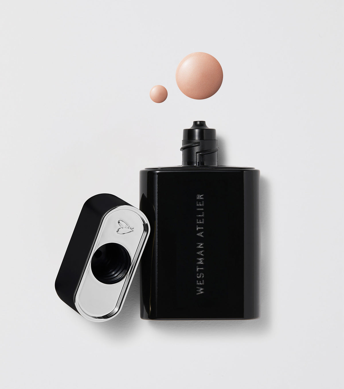 A black bottle of Westman Atelier Liquid Super Loaded Tinted Highlighter with its cap removed, showing a small amount of product headphone on a white background.