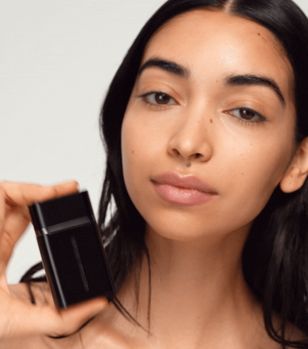 A black bottle of Westman Atelier Liquid Super Loaded Tinted Highlighter with its cap removed, showing a small amount of product headphone on a white background.