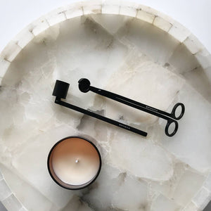 Round marble tray with a candle and two black candle sticks on a light gray background
