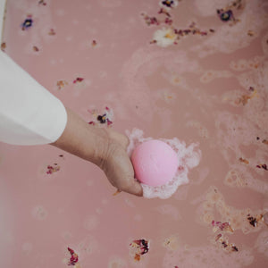A person holding a ink bath bomb above a botanical bath