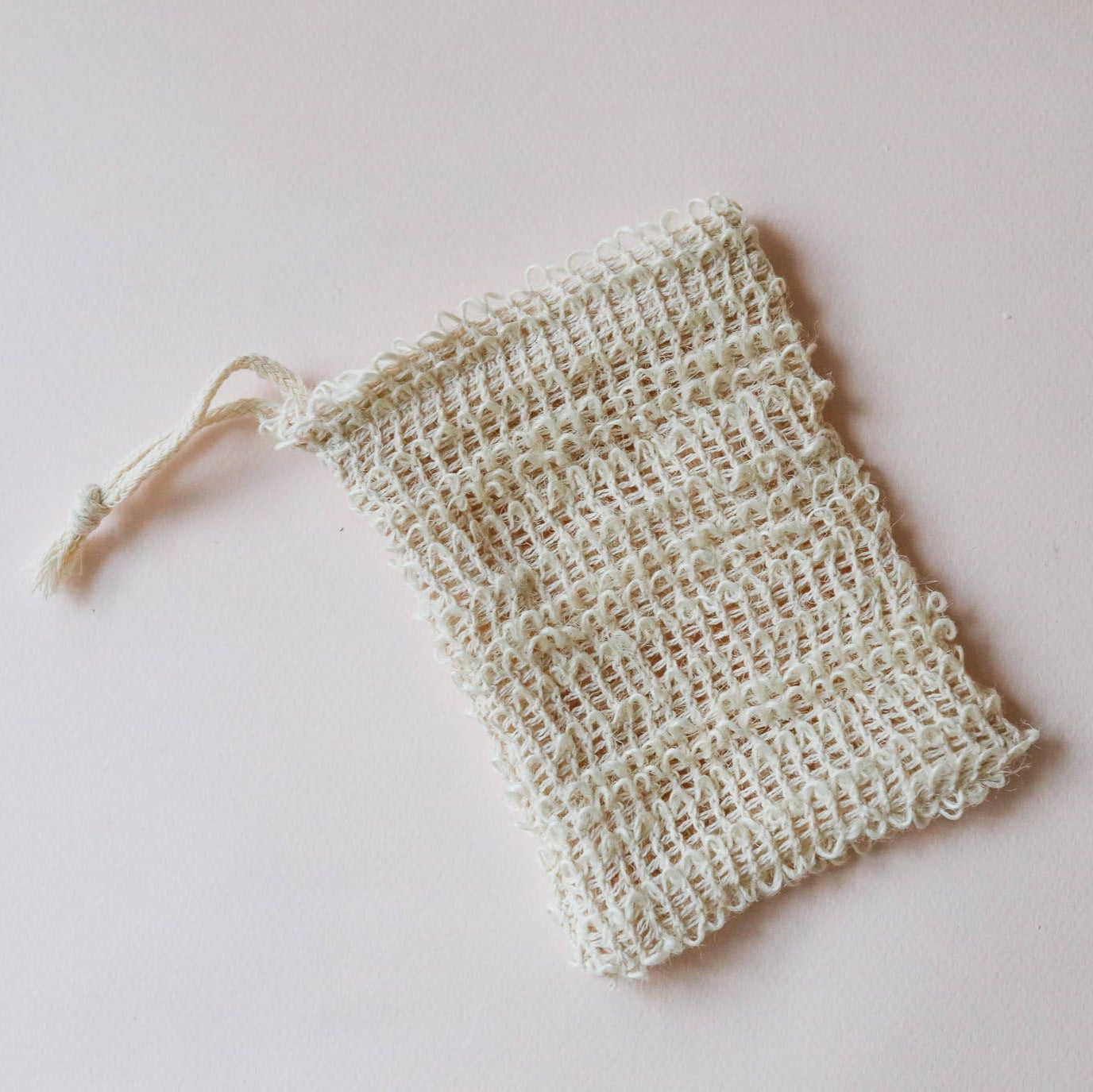 A bar of soap placed inside a beige, agave fiber soap saver pouch with the label 'MUMU BATH' on top, secured with a twine loop.