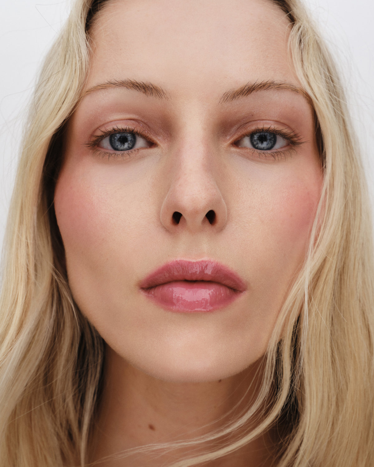 A photo of Westman Atelier Squeaky Clean Liquid Lip Balm with the container to the left and the applicator wand to the right, showing a translucent pink color.