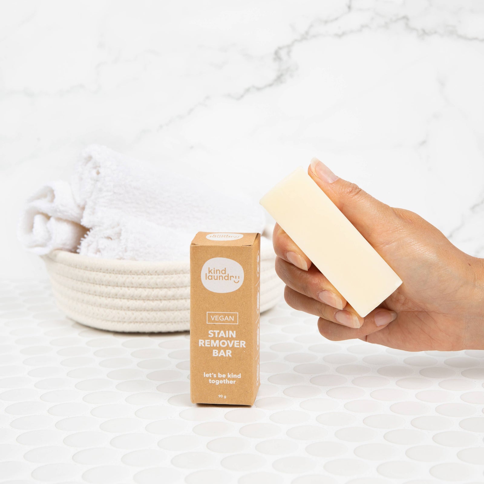A person holding a stain remover bar on a tile surface, in front of a marble background. 
