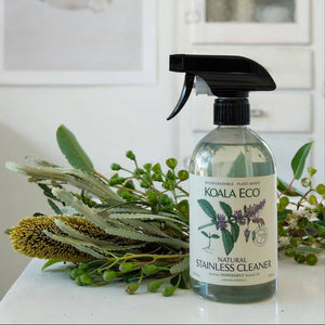 A bottle of Koala Eco Stainless Cleaner on a white counter with a bunch of greenery and flowers lying beside it
