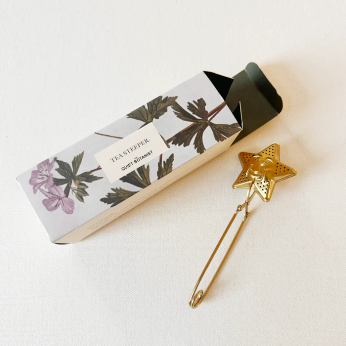 Gold star-shaped tea infuser with packaging on a white background