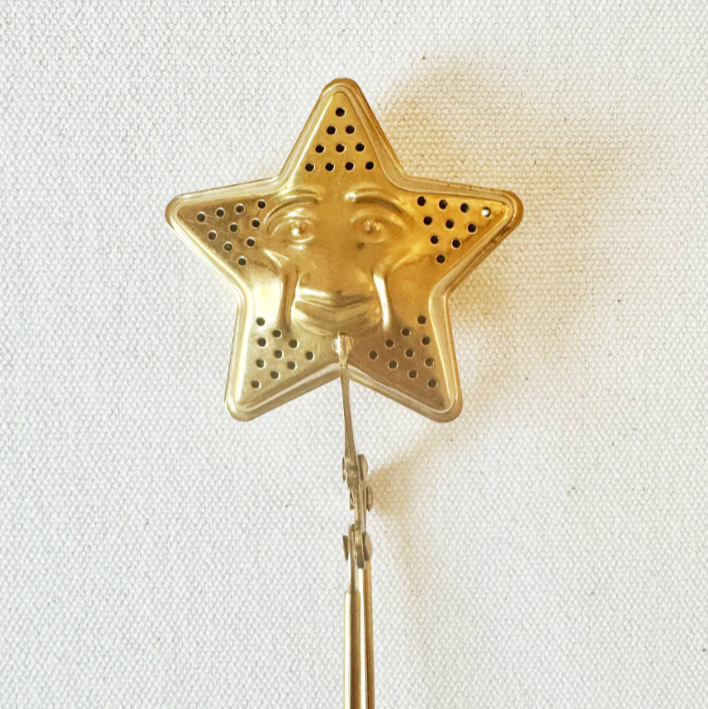 Gold star-shaped tea infuser with packaging on a white background