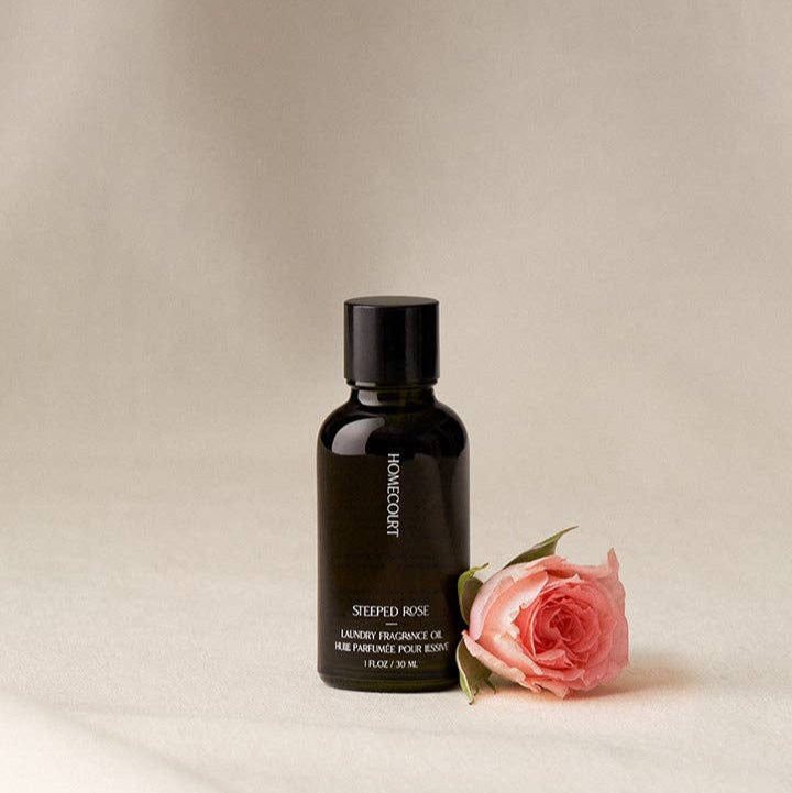 Black bottle of Homecourt Steeped Rose fragrance oil with a pink rose on a beige background