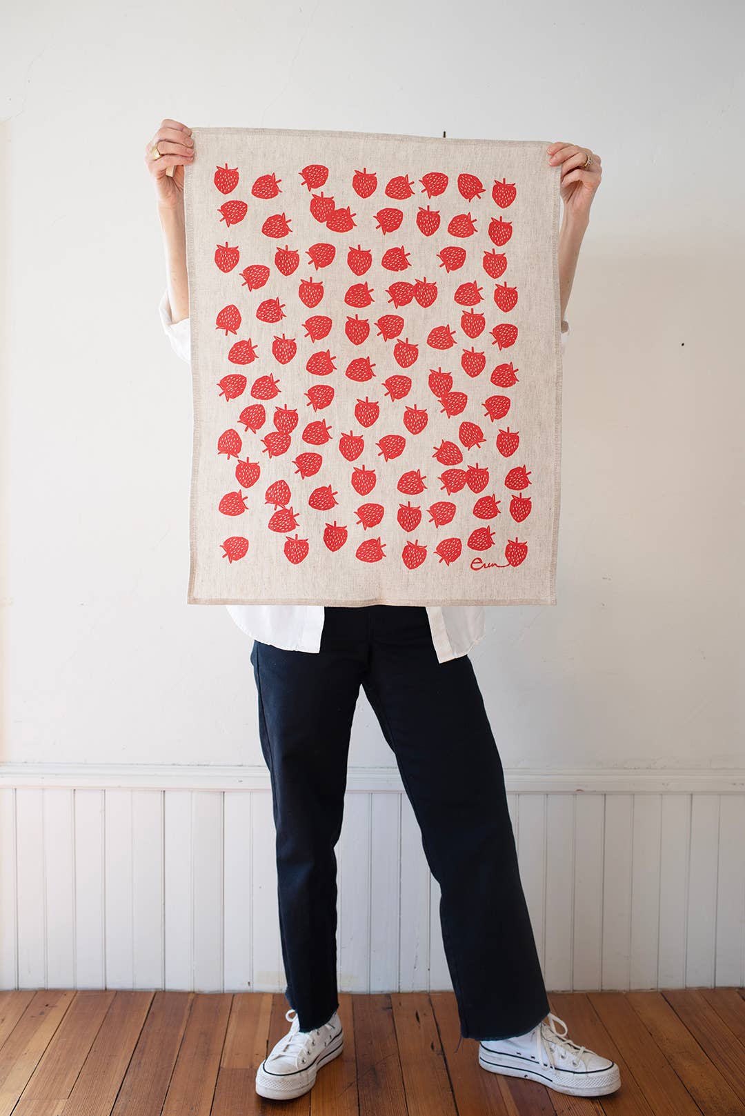 Person holding a tea towel with red apple pattern against a white wall.