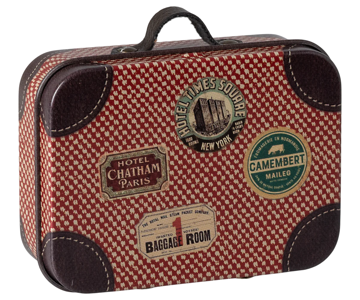 Small metal suitcase with a red and beige checkered pattern and decorative travel stickers such as 'Hotel Chatham Paris' and 'Bagage Room'.