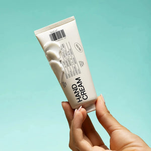 Hand holding a tube of hand cream against a light blue background