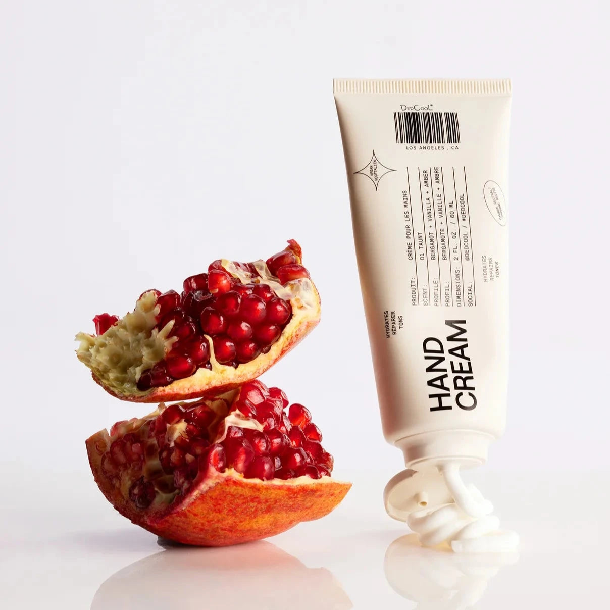 Hand cream tube next to a pomegranate on a white background