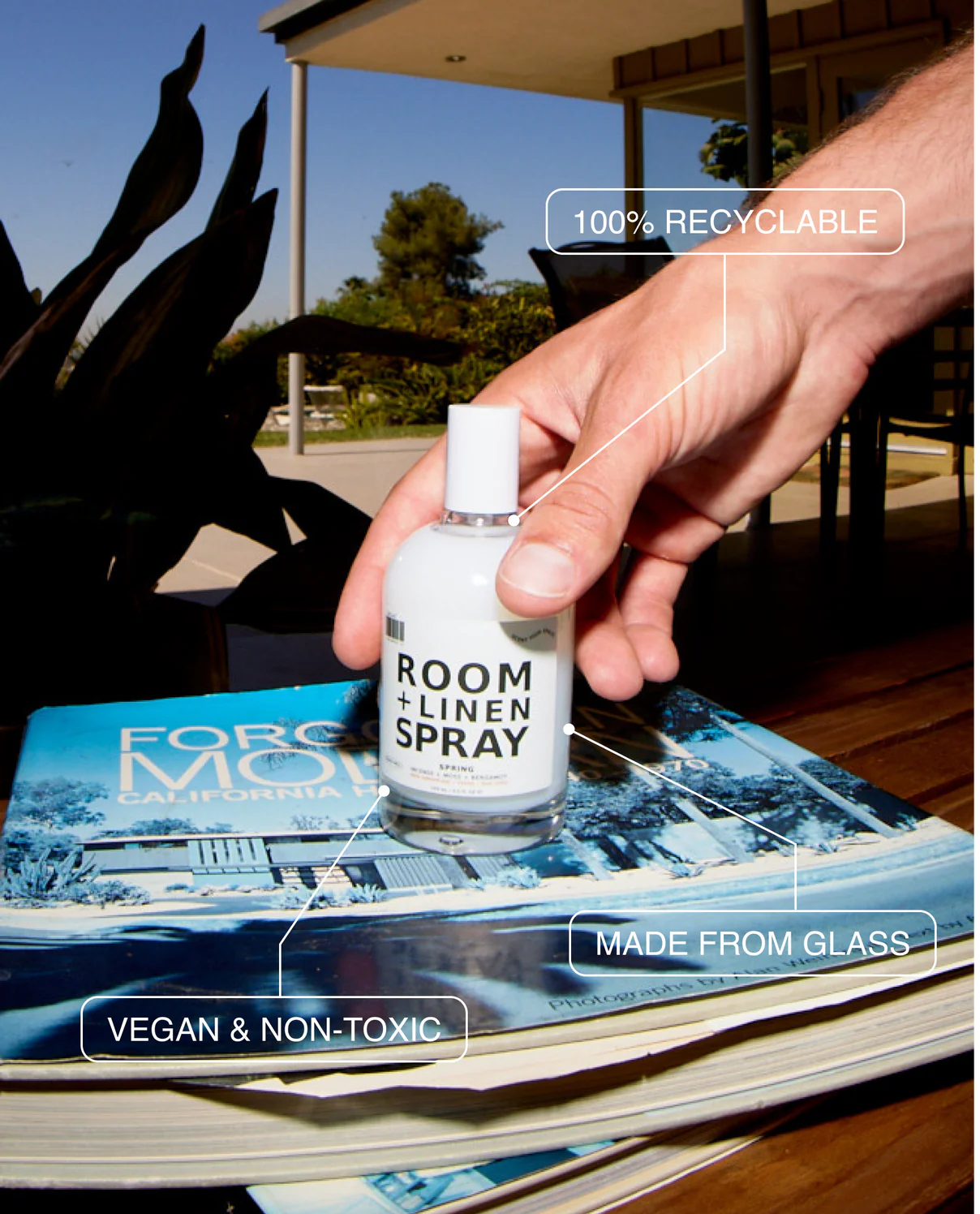 Hand holding a room and linen spray bottle on a magazine with outdoor background