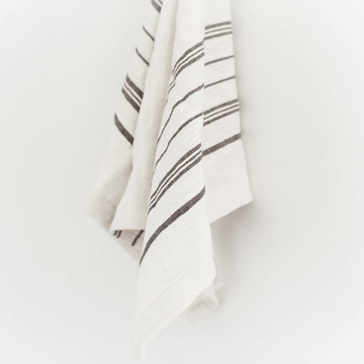 A white tea towel with grey stripes on a white background. 
