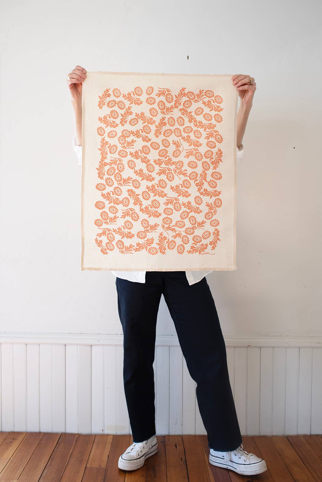 Person holding a tea towel with orange floral designs on it, against a white wall