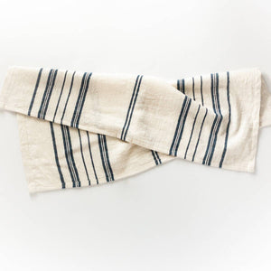 A white tea towel with blue stripes on a white background. 