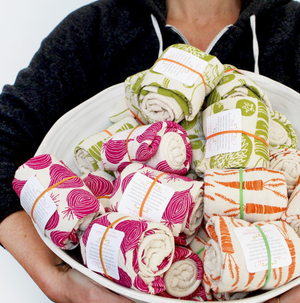 A person holding a bowl of Noon Designs tea towels.