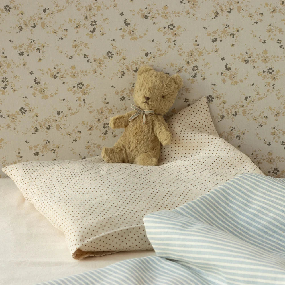 A small, plush teddy bear with a vintage look, sitting next to its packaging box which is also styled with vintage graphics.