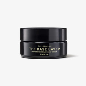 A black jar with a gold and white label reading 'THE BASE LAYER' by Caldera + Lab, indicating a nourishing day moisturizer.