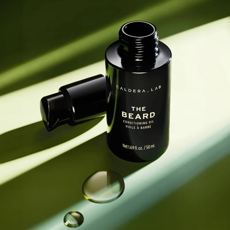 A black pump bottle labeled 'THE BEARD' by Caldera + Lab, which is a conditioning oil for beard and skin.