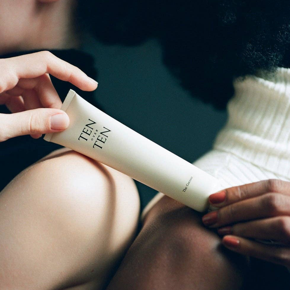 Person holding a tube of skincare product labeled 'TEN' on a blurred background