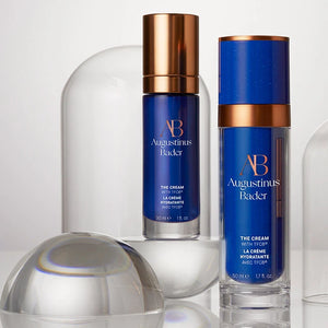 Two bottles of Augustinus Bader skincare cream with blue and bronze design on a white background.