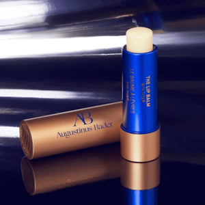 Augustinus Bader lip balm with blue and bronze design on a reflective surface