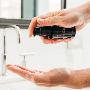 A person pumping the smooth into their hand in front of a sink. 