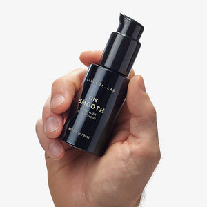 A person holding a small black bottle labelled The Smooth