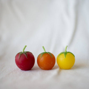 Three small fruits, one red, one orange, and one yellow, on a white fabric background.