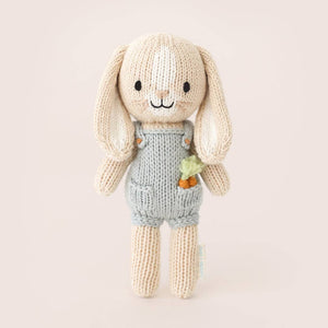 A small knit bunny wearing blue overalls with carrots in its pocket. 