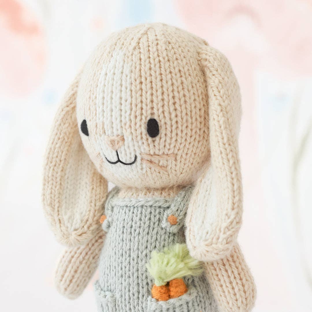 A detail of a small knit bunny wearing blue overalls with carrots in its pocket. 