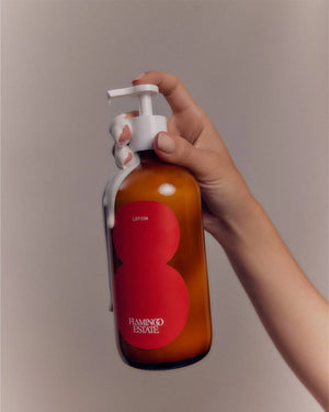 A person holding a brown bottle of Flamingo Estate tomato lotion