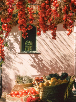 A light pink structure sitting behind baskets of fresh produce and hanging tomato plants overhead
